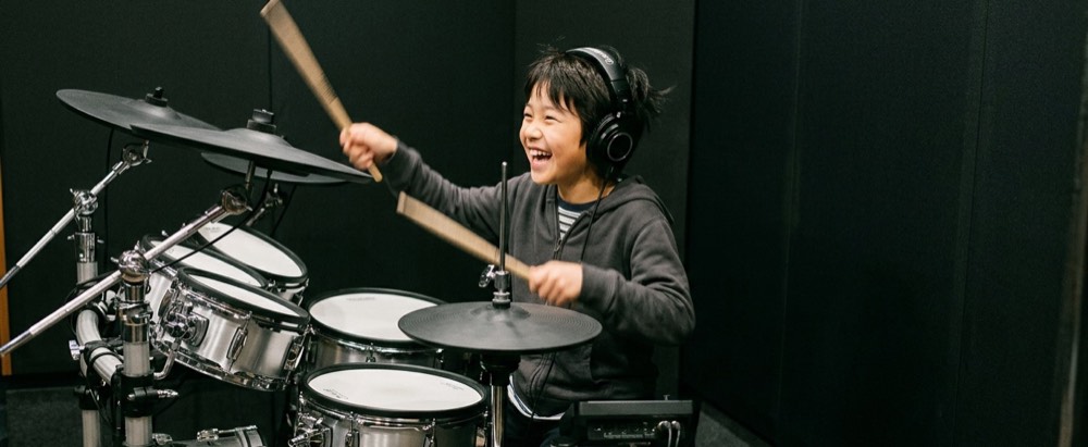 ヘッドホンを付けて電子ドラムを叩く子ども